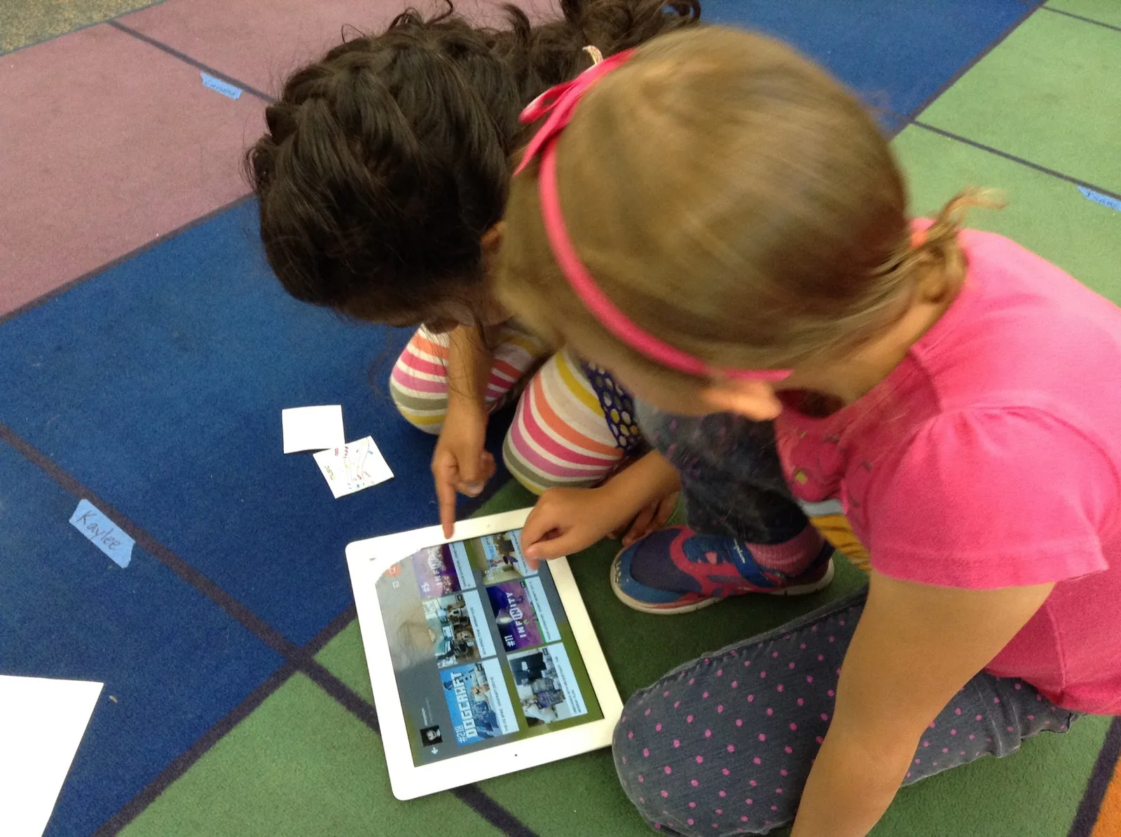 Two kids in a co-design session, one tapping an iPad on the floor beside paper drawings