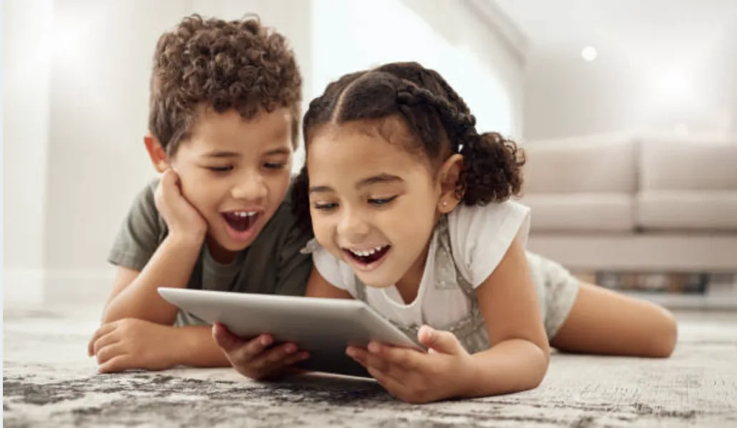 Two kids lying on the floor, laughing at a tablet